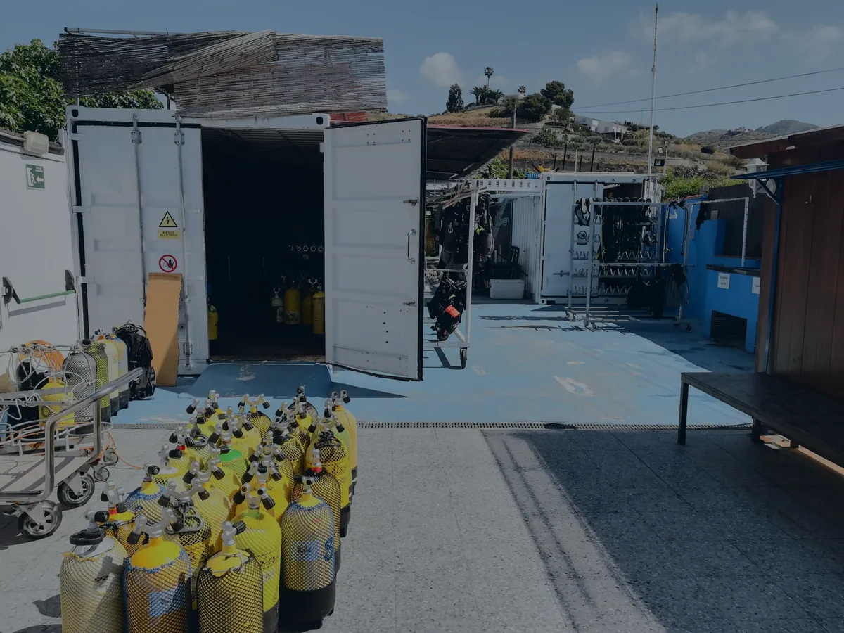 El patio del centro: las botellas amarillas agrupadas en el suelo, el contenedor del material abierto y los trajes colgados al fondo.