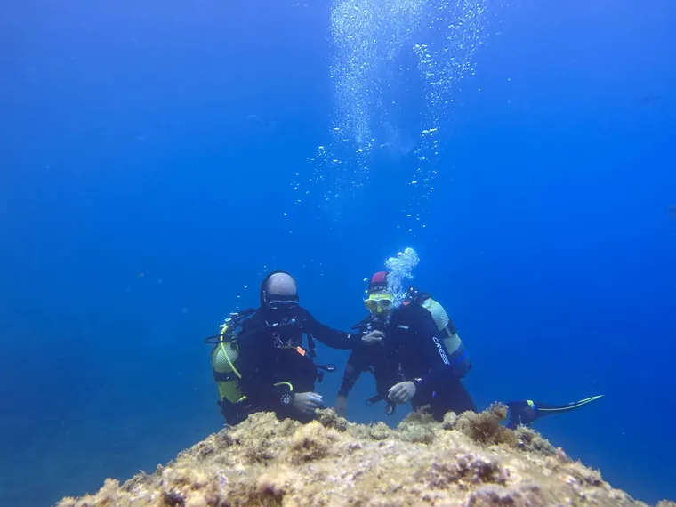 Instructor y buceadora se miran junto a una roca en el agua azul